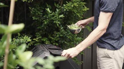 Man puts vegetable scraps into compost tumbler, obscured medium shot