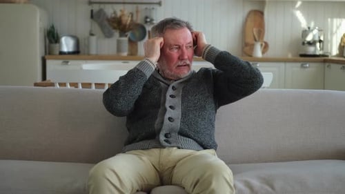 Man Massages Temples on Couch Due to Head Pain