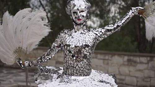 Woman in reflective mirror costume dancing with feather fans. Street performer show.