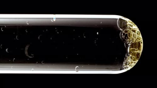 Foto macro de bolhas douradas de diferentes tamanhos descendo em tubo de ensaio de vidro sobre fundo preto