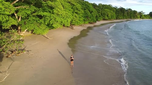 Woman walking over tropical beach and panning the drone around the landscape in Costa Rica.