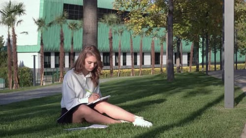 Young Attractive Female Student Studying Outdoors Against the Backdrop of a College