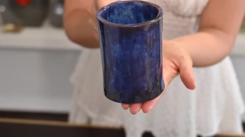 Woman in white dress showing a blue cup, final result at pottery workshop