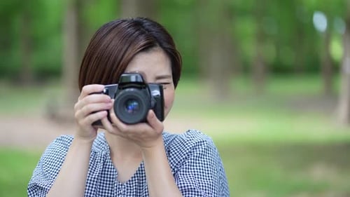 Smiling Woman Taking Pictures With a Camera in Park