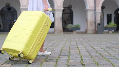 Closeup of a Yellow Suitcase Being Pulled By a Young Leggy Girl Along the Cobblestones in the City