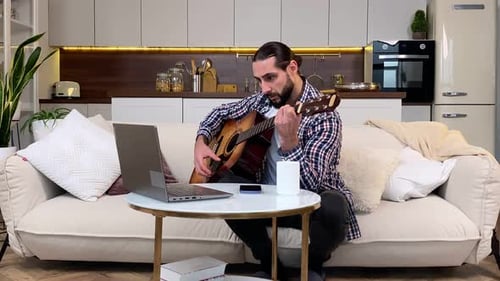 Man Playing Guitar at Home with Laptop