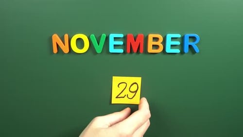 Hand sticking a sticker 29 November calendar day on school board. 29 date of November. Twenty ninth