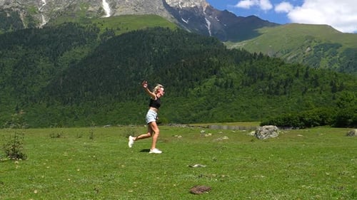 Young woman running through a field with mountain scenery