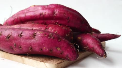Close Up of Raw Sweet Potato on Chopping Board on White Background