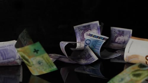 Different money in different currencies falls on a black mirroring surface in slow motion.