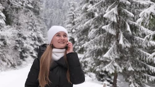 Happy Girl Walks Through a Snowy Forest and Talks on the Phone