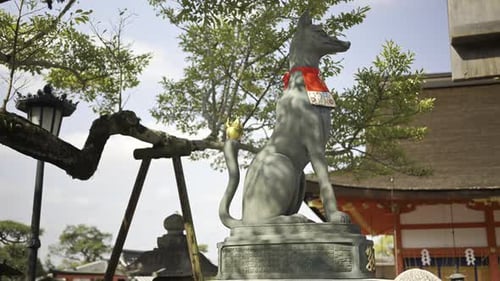 A graceful fox statue stands proudly at Fushimi Inari traditional Japanese shrine, decorated with a