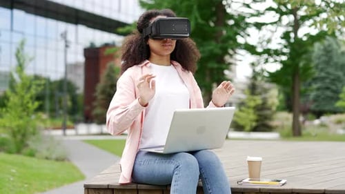 African american female student works using VR glasses in virtual reality simulator sitting on bench