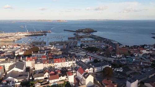 High circling flight over rooftops of St Peter Port Guernsey centring on harbour and Castle Cornet