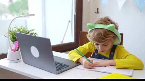 Child Writing in Notebook with Laptop and Headphones