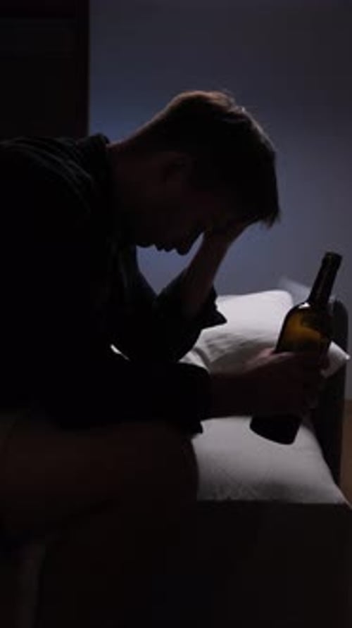Despondent Young Man Sits with Wine in Dark