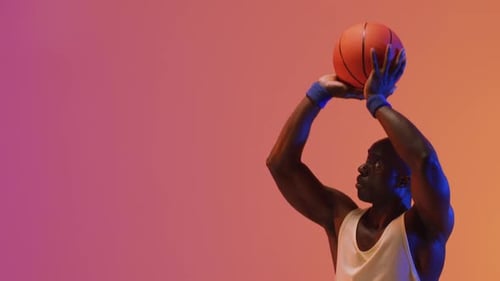 Video of african american male basketball player throwing ball on pink to orange background