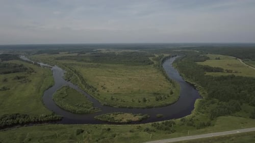 Aerial View of a Bending River Flowing and Crossing Wide Green Field Stock Footage Summer Rural
