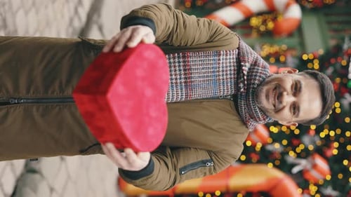 Vertical Video Caucasian Bearded Man Standing in the Winter Decorated Street Holding the Valentino