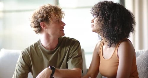 Couple assis sur un canapé près de la fenêtre, une femme initiant une conversation, se penchant et partageant une histoire