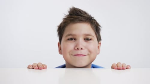 Smiling Boy Peeking Over White Table