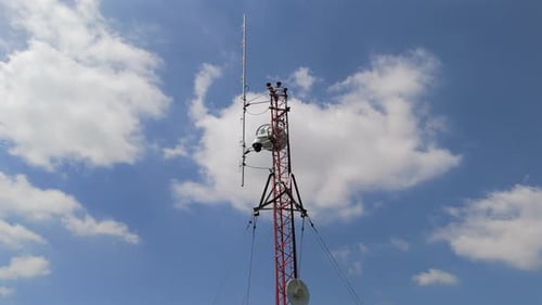 Communication tower standing against the sky, aerial orbit with a cloudy blue sky backdrop