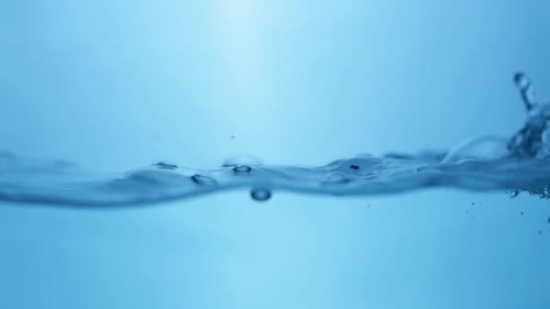 Waves of clear water splattering and creating tiny droplets as it ripples inside a container.