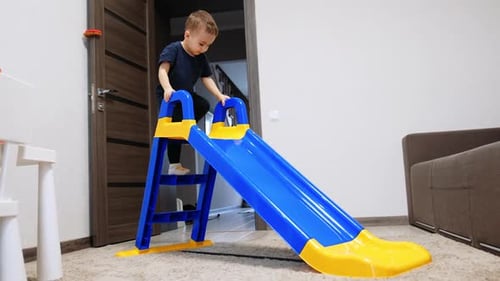 Active Caucasian toddler climbing and sliding from a slide. Cute baby having fun at home.