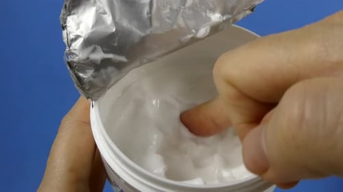 Close-up video of a classic round jar filled with glossy white cream, placed on a clean solid blue b