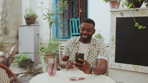 Smiling Man Using Smartphone at Outdoor Cafe