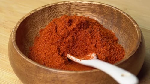 Paprika powder spice in wooden bowl with spoon rotating on wooden board. Dry seasoning in spoon