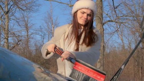 Woman Brushing Snow Off Car in Winter Forest
