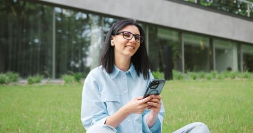 Attractive young woman with a beautiful smile sitting cross-legged on the grass in a green park