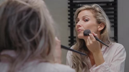Woman Applies Makeup with Brush in Mirror