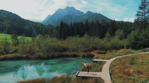 Wide shot of beautiful female doing yoga on her mat in magical nature at a mountain lake.