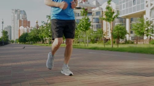 Closeup of Male Legs in Sports Shoes Jogging in City Street at Sunrise