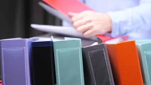 Office Worker Reading Documents with Colorful Ring Binders in the Foreground