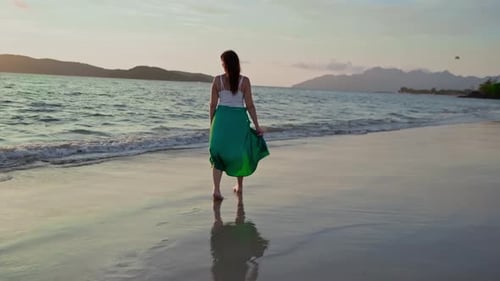 Young Woman Walking Barefoot on Sandy Beach at Sunset
