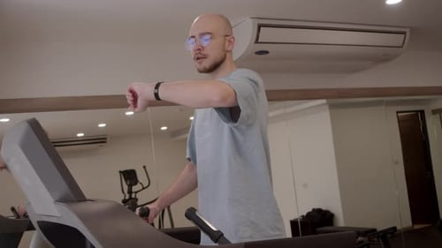 Man Doing Treadmill Workout at Gym Briefly Checking Smartwatch or Fitness Band for Calorie Count and
