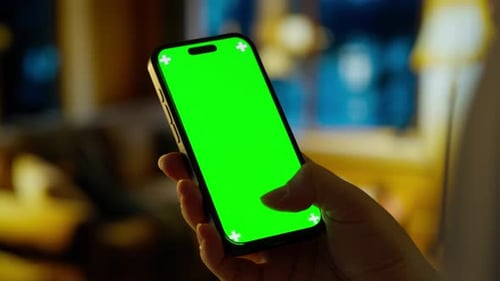 Person Holding Smartphone with Bright Green Chroma Key Screen in Cozy Indoor Setting Showcasing