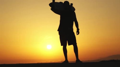 Silhouette of a Man Standing on Sunset and with a Longboard on His Shoulder