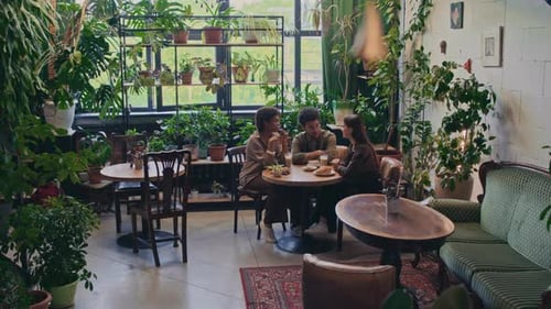 Diverse Young Students Chatting at Table in Stylish Verdant Cafe