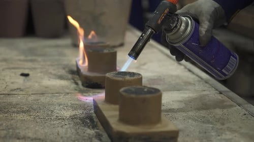 Foundry Worker Using Blowtorch on Small Clay Cylinders Stock Clip