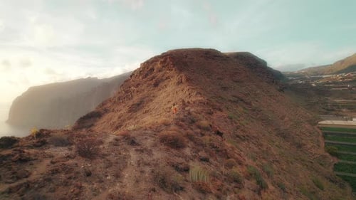 Person running along rocky hills at dusk, with a panoramic view of rugged cliffs and ocean under a h