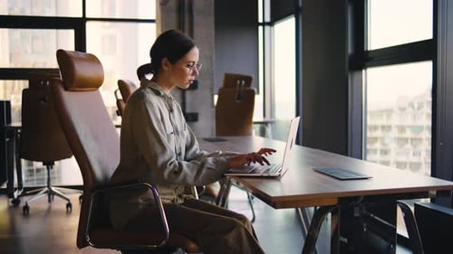 A Professional Woman is Working Diligently at a Modern Office Desk Equipped with a Laptop Enjoying a