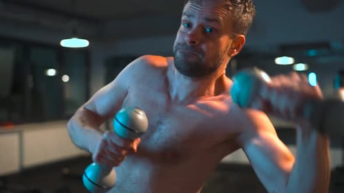 Boxer Practices Punches with Dumbbells in His Hands in the Gym in the Evening