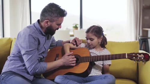 Man teaching girl to play guitar on sofa
