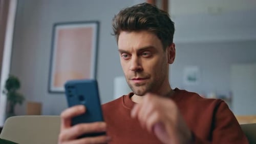 Nervous Student Swiping Mobile Phone Reading Bad News on Couch Home Close Up