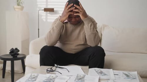 Frustrated Man Sitting with Bills on Living Room Couch