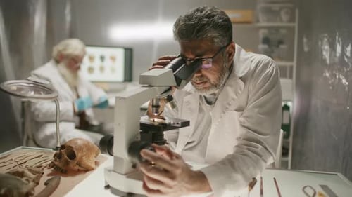 Mature Scientist Examining Specimen under Microscope in Archaeology Laboratory